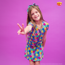 Load image into Gallery viewer, Young girl wearing a colorful dress with smiley face patterns on a purple background