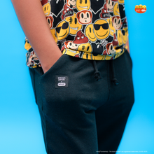 Load image into Gallery viewer, Person wearing a colorful sleeveless shirt with cartoon characters and dark pants on a blue background