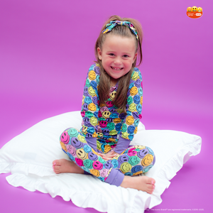 Child wearing a colorful emoji-themed outfit sitting on a white pillow against a purple background