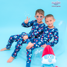 Load image into Gallery viewer, Two children wearing blue pajamas with red and white patterns, sitting on a blue background with a Smurf toy.