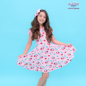 Girl wearing a pink dress with cherry pattern on a blue background, featuring the Smurfs brand.