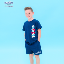 Load image into Gallery viewer, Child wearing a blue &#39;Smurfs&#39; themed t-shirt and shorts on a light blue background