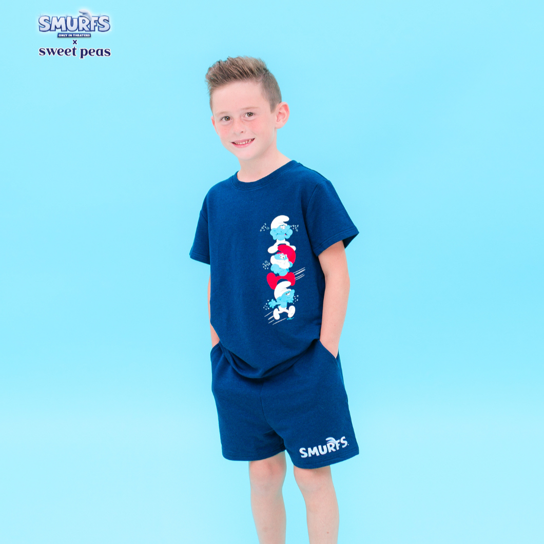 Child wearing a blue 'Smurfs' themed t-shirt and shorts on a light blue background