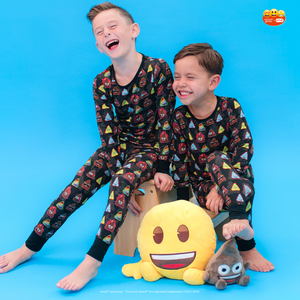Two children wearing matching pajamas with emoji patterns on a blue background.