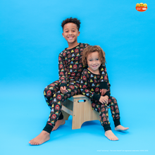 Load image into Gallery viewer, Two children wearing matching pajamas sitting on a wooden stool against a blue background.