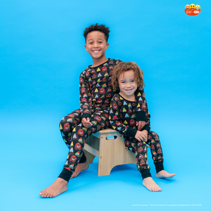 Two children wearing matching pajamas sitting on a wooden stool against a blue background.