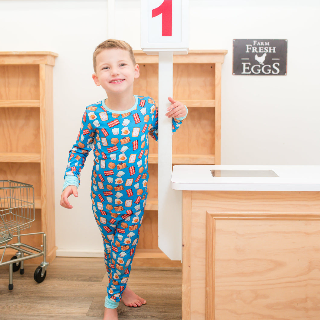 Child in colorful pajamas standing in a kitchen with wooden cabinets and a sign in the background.