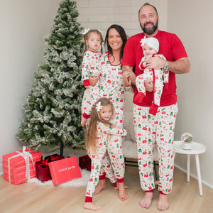 Family of four in matching Christmas pajamas standing in front of a decorated Christmas tree.
