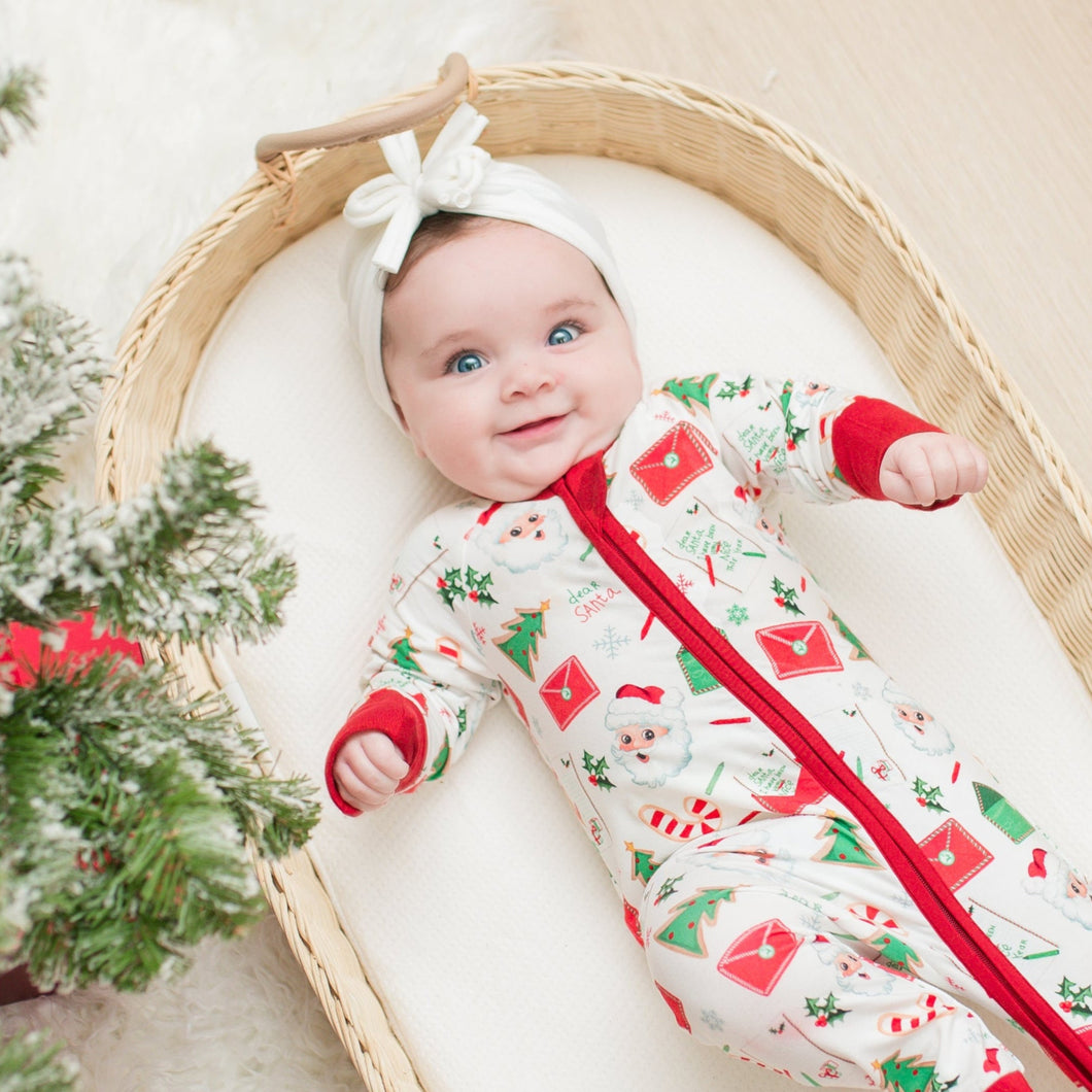Baby in a festive outfit lying in a basket next to a decorated Christmas tree.