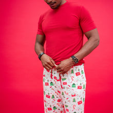 Load image into Gallery viewer, Person wearing a red shirt and Christmas-themed pajama pants against a red background