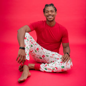 Man wearing a red t-shirt and white patterned pants sitting on a red background