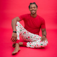 Man wearing a red t-shirt and white patterned pants sitting on a red background