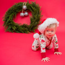 Load image into Gallery viewer, Baby in Christmas pajamas and hat on a red background with a wreath.