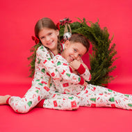 Two children in matching Christmas pajamas sitting on a red background with a wreath.