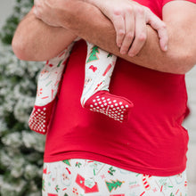 Load image into Gallery viewer, Person wearing Christmas-themed pajamas holding a child&#39;s foot with a Christmas tree in the background