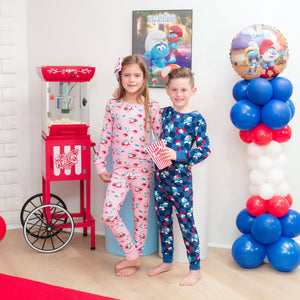 Two children in pajamas standing in front of a candy machine and balloon decorations.