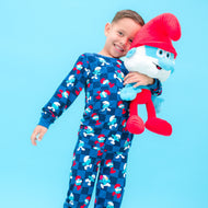 Child wearing a blue pajama set with cartoon characters, holding a red plush toy against a light blue background